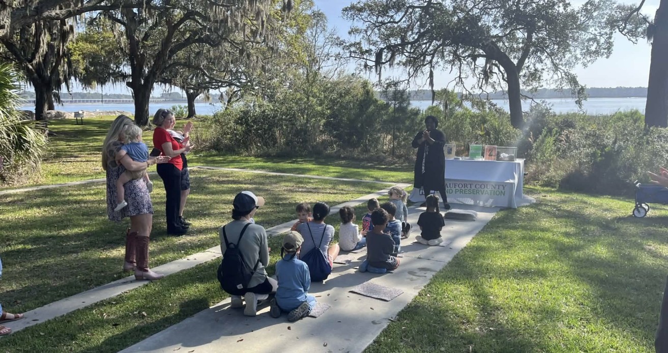 Young children and their caregivers enjoy a scenic storytime near the waterfront at Fort Frederick in Beaufort, SC.