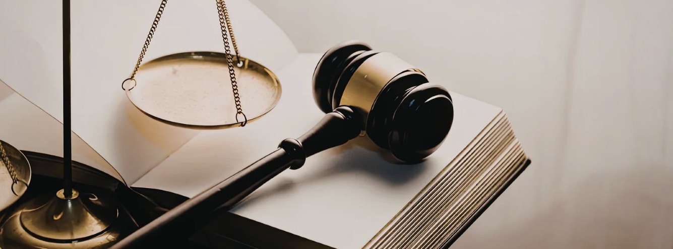 A gavel rests on an open law book next to a brass scale.