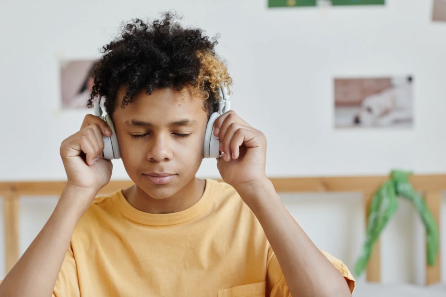 Teen boy with eyes closed listening to headphones in a room.